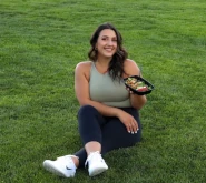 Picture of owner - Cynthia Loza. She is a lightly tanned hispanic girl; sitting on the grass. Holding up a delicious meal with a smile.